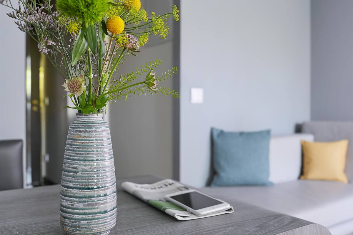 A modern room with a grey sofa, a yellow pillow, a blue pillow, and a white smartphone on a wooden table.