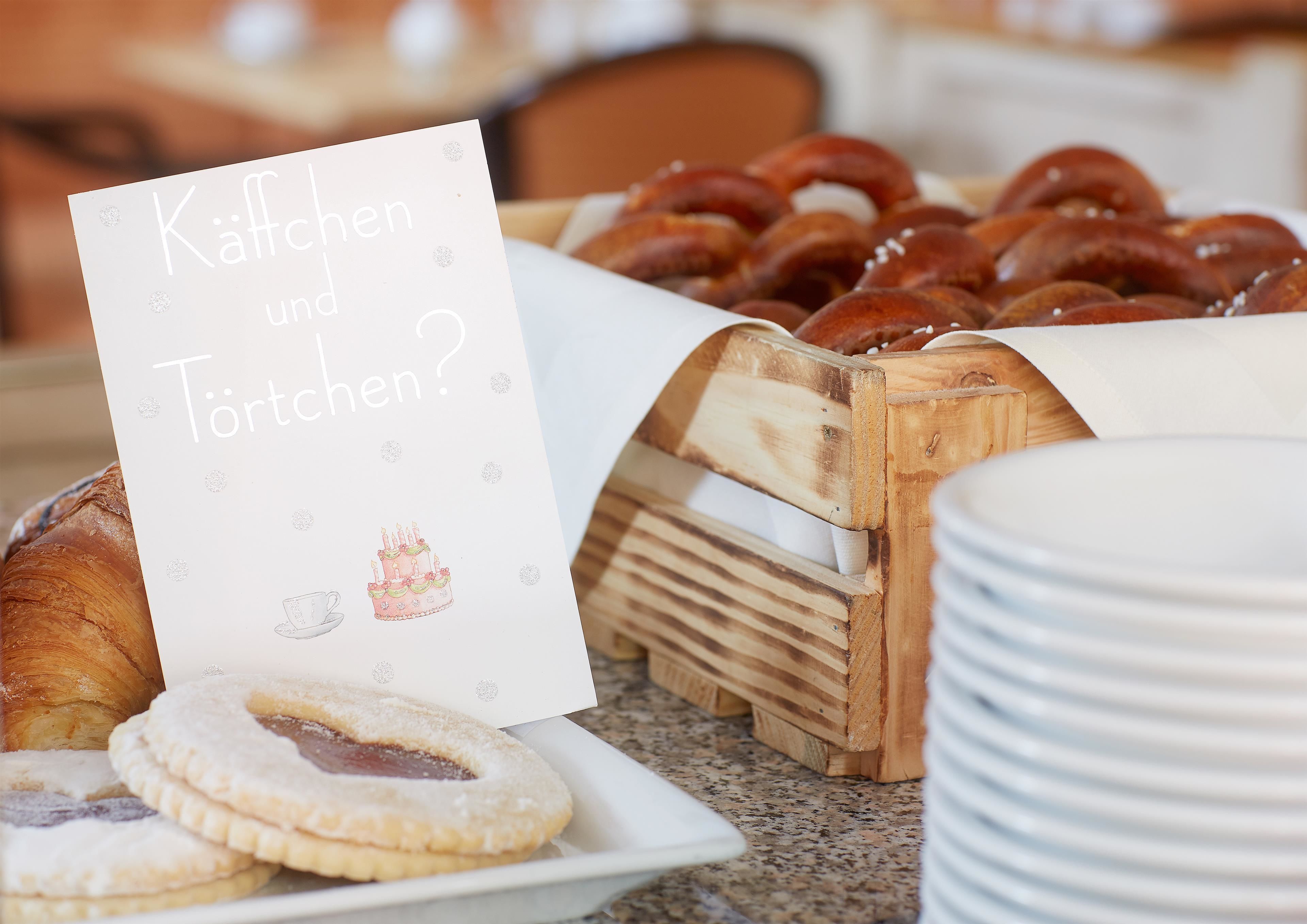 A breakfast buffet with pastries, a cake, and a sign asking about coffee and tea.