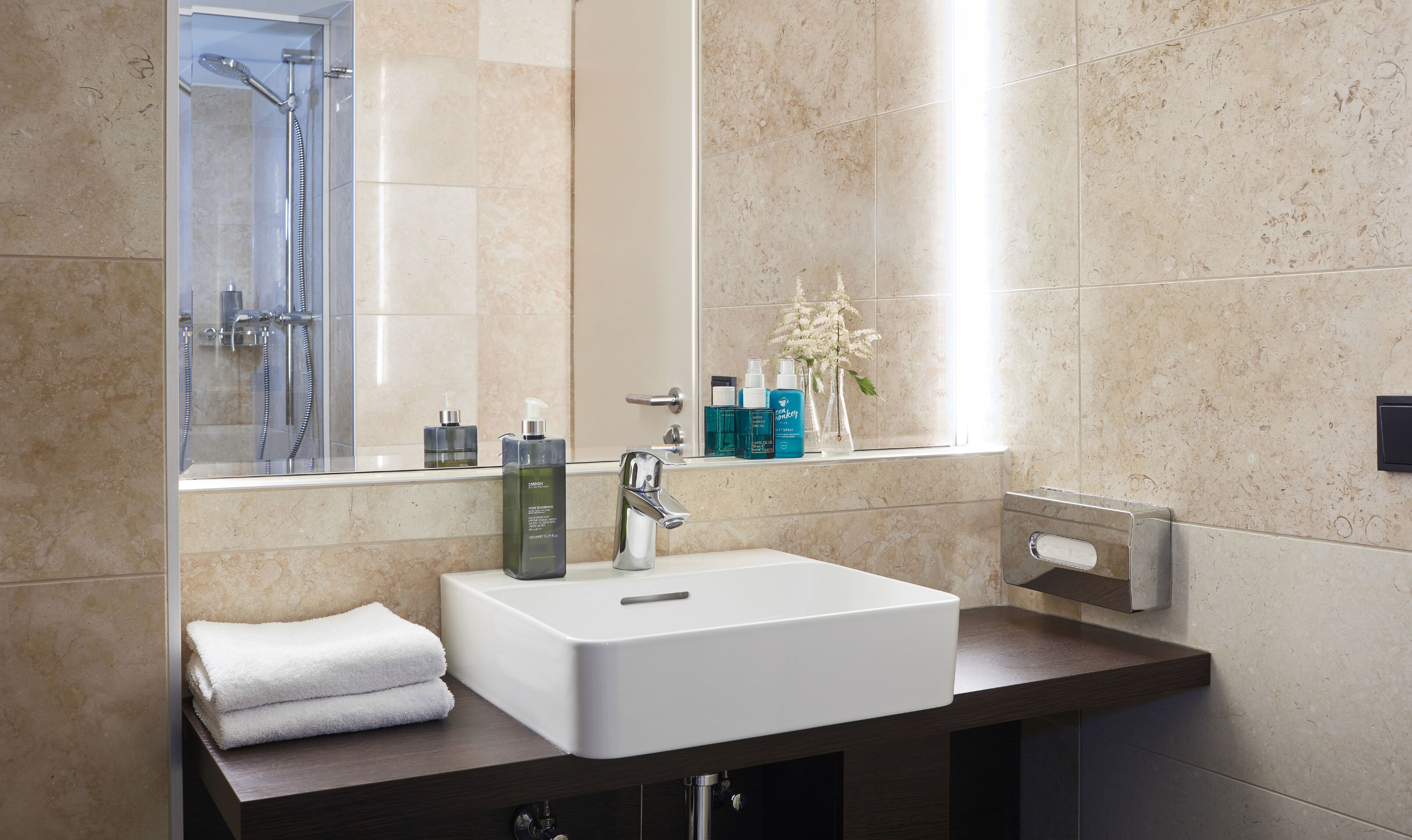 A modern bathroom with a white sink, a glass shower enclosure, and toiletries on the vanity.