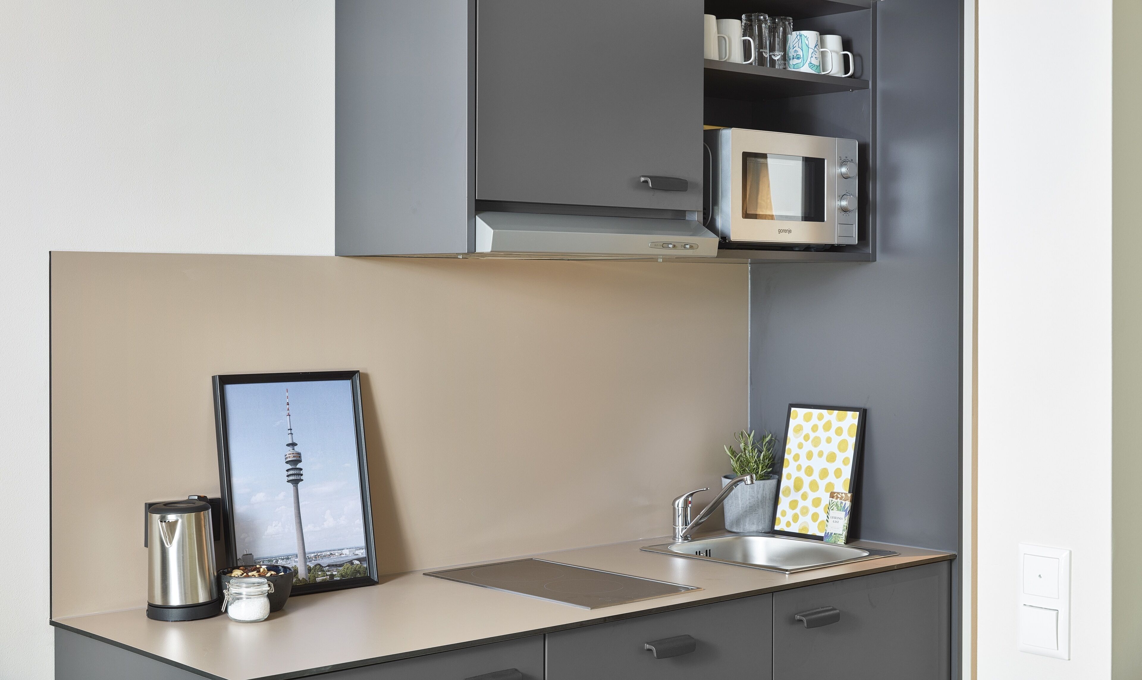 Cocina moderna con microondas integrado, un lavamanos y un cuadro con una vista urbana enmarcada.