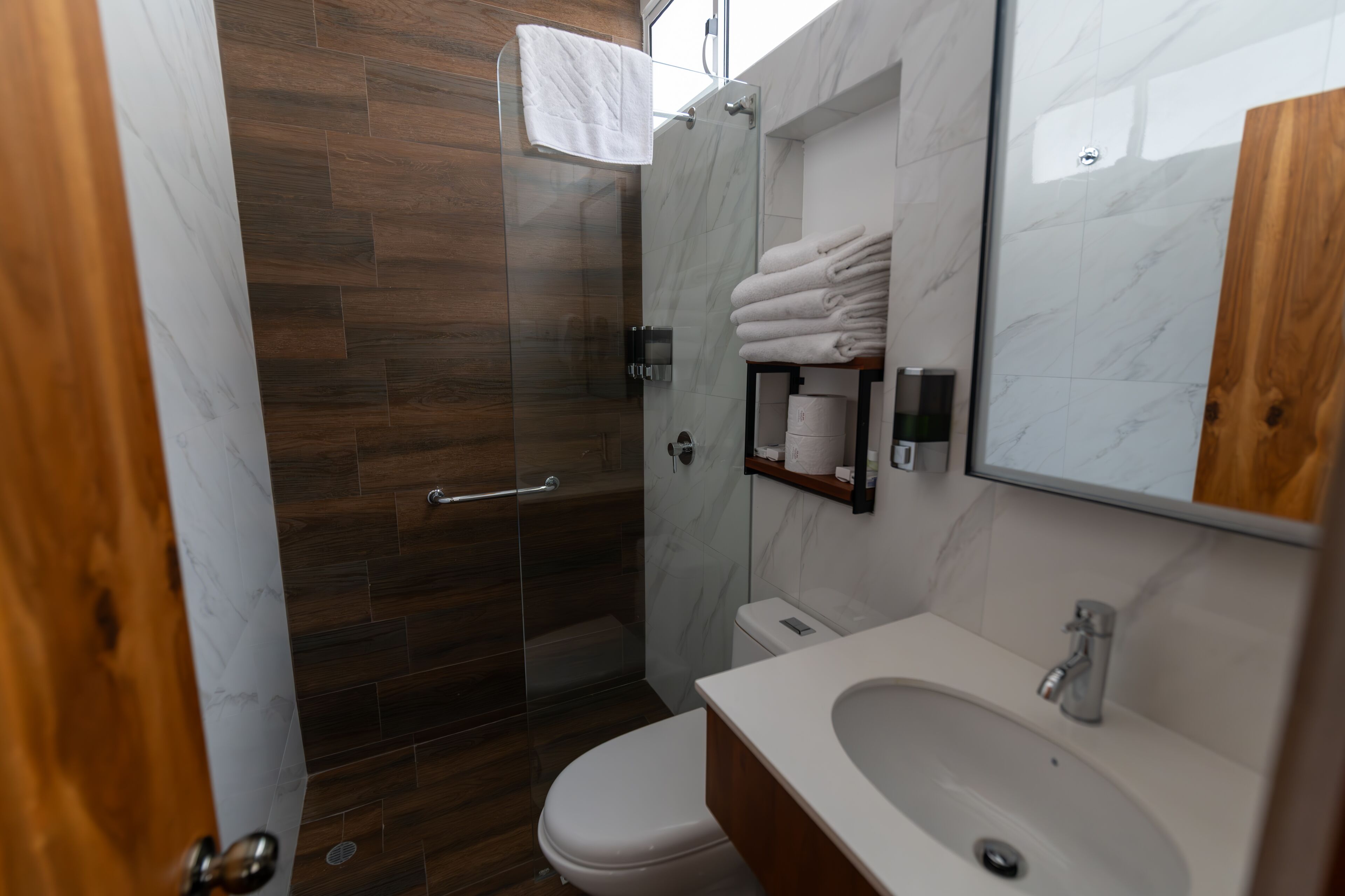 A modern bathroom with a glass-enclosed shower, a white toilet, and a vanity with a sink and mirror.