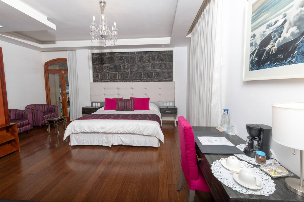 Una habitación de hotel con una cama grande, un escritorio con silla, una cafetera y un cuadro en la pared.