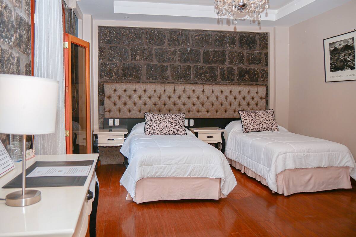 Habitación de hotel con dos camas, un candelabro, una pared de piedra y un cuadro en la pared.