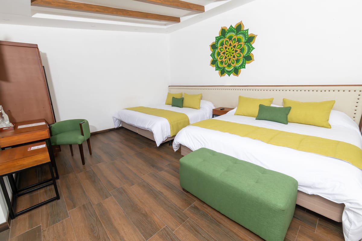 Habitación de hotel con dos camas, un escritorio y una silla verde.