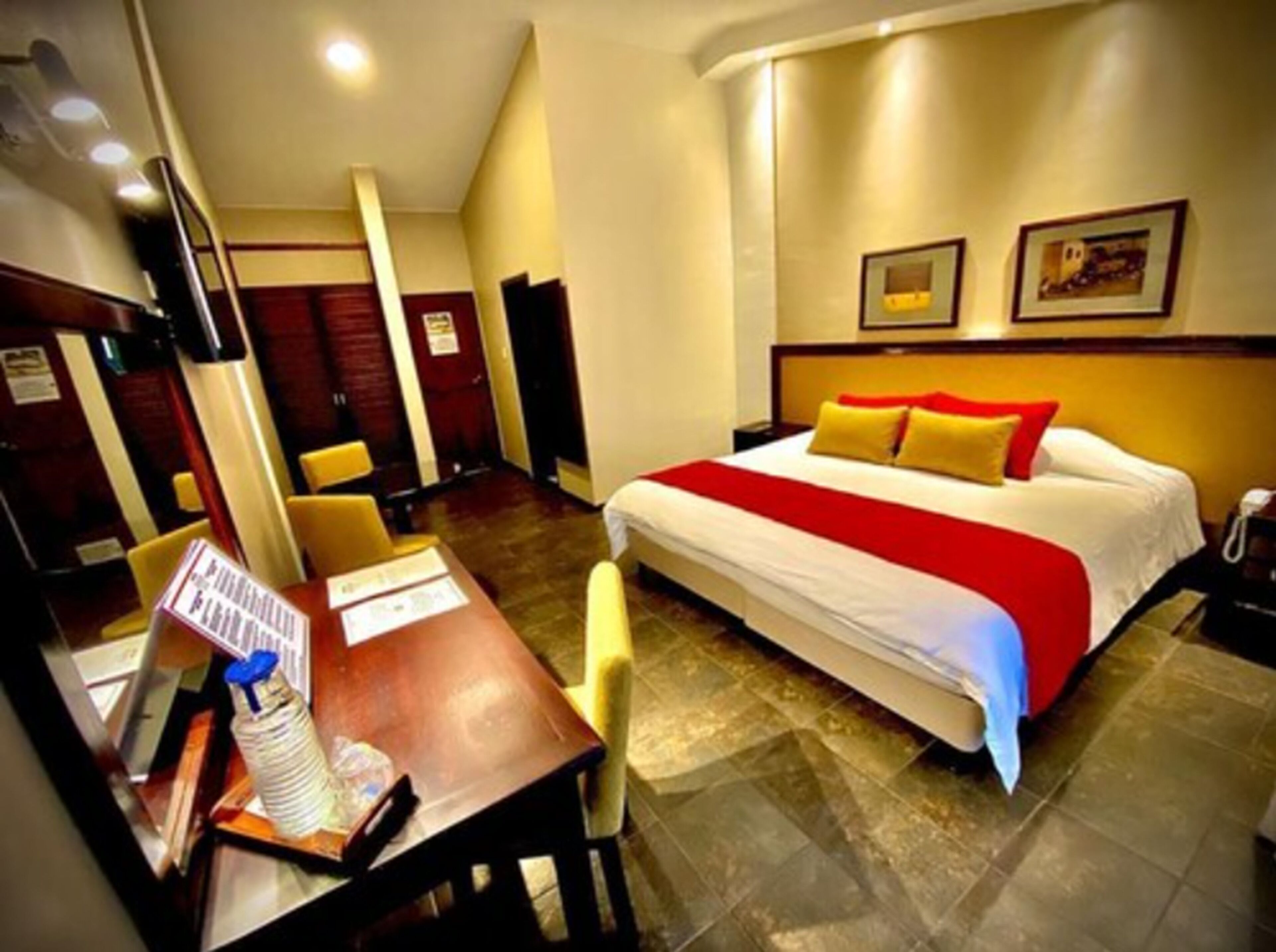 A hotel room with a bed, a desk with a chair, a telephone, and a picture frame on the wall.