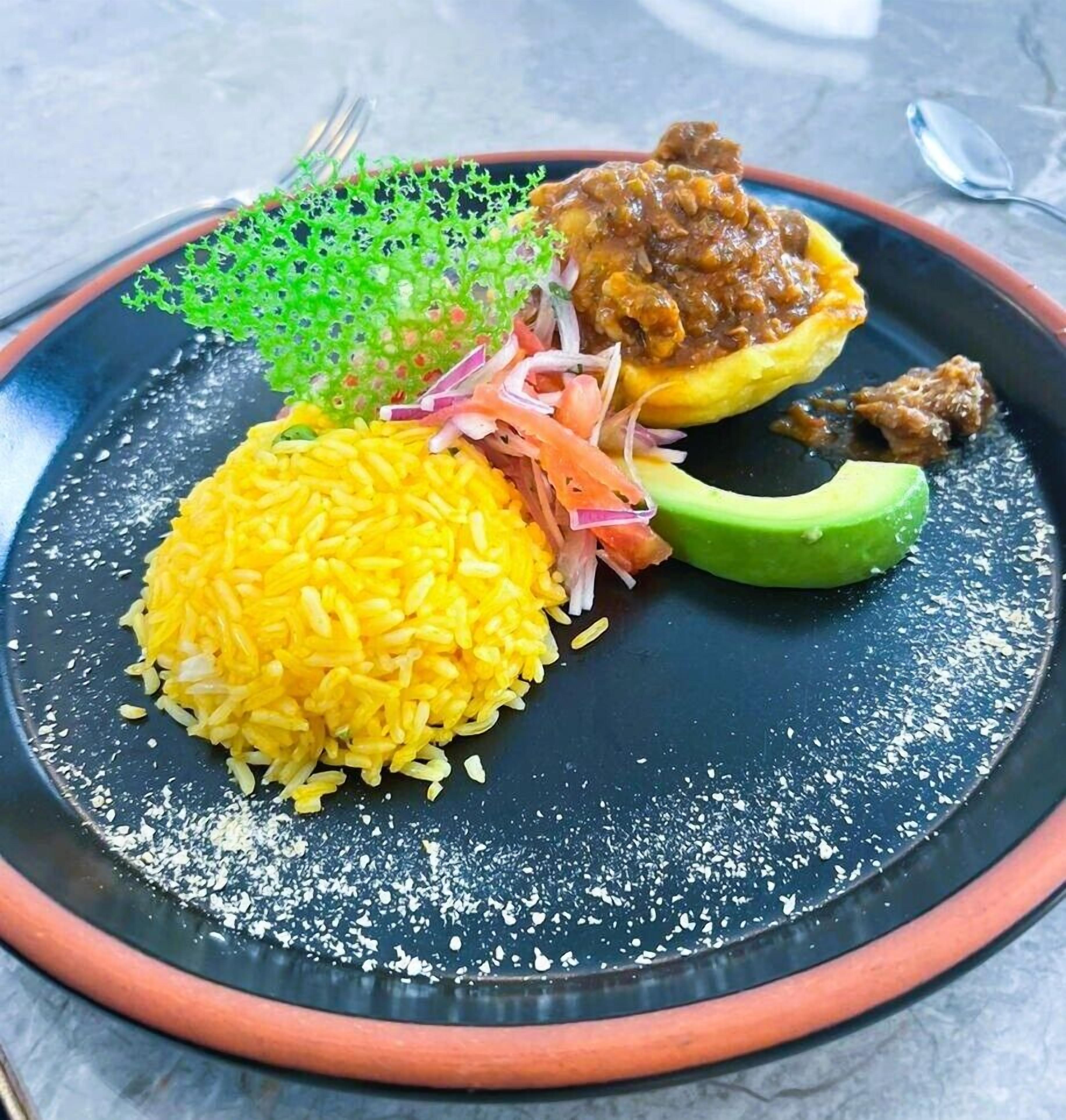 A plate with yellow rice, a stuffed pepper, and a slice of avocado.