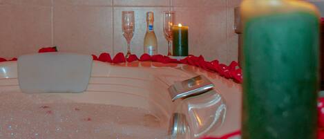 Una bañera con pétalos de rosa, una vela y una botella de champán.