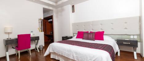 A bedroom with a large bed, a desk, a chair, and a wardrobe.