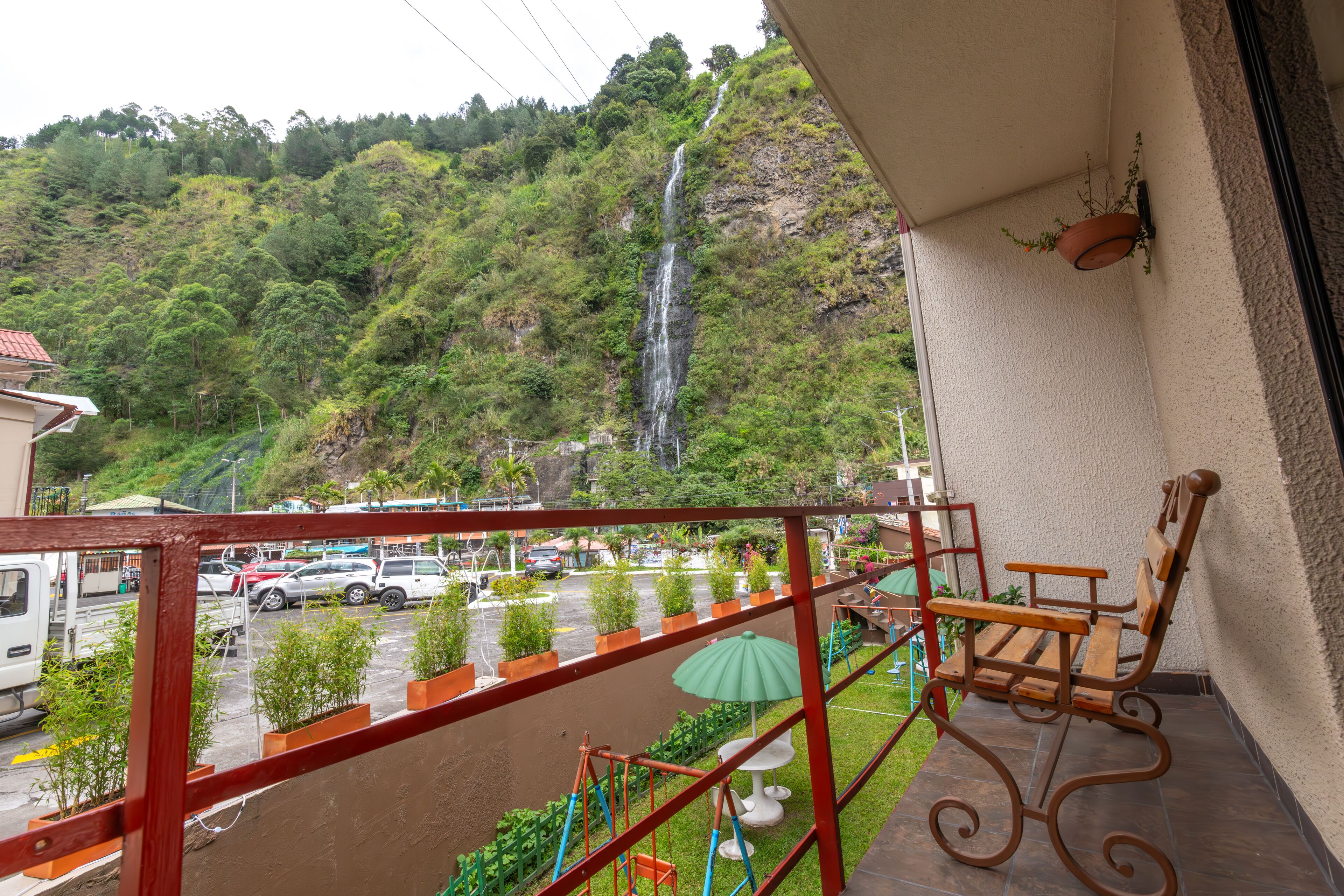 Un balcón con vista a una cascada, un estacionamiento y un césped verde con plantas en macetas.