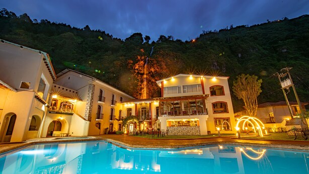 Un hotel con piscina, varios balcones y un paisaje montañoso de fondo.