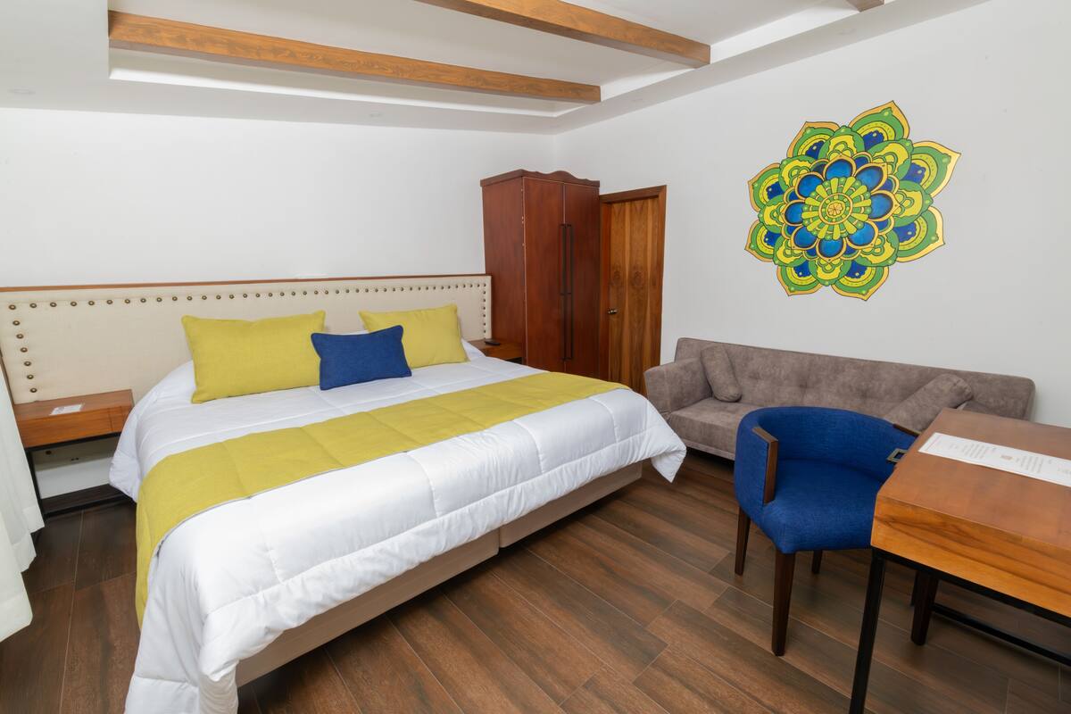 Un dormitorio con una cama, un armario de madera, un sofá, un sillón azul y una mesa de madera.