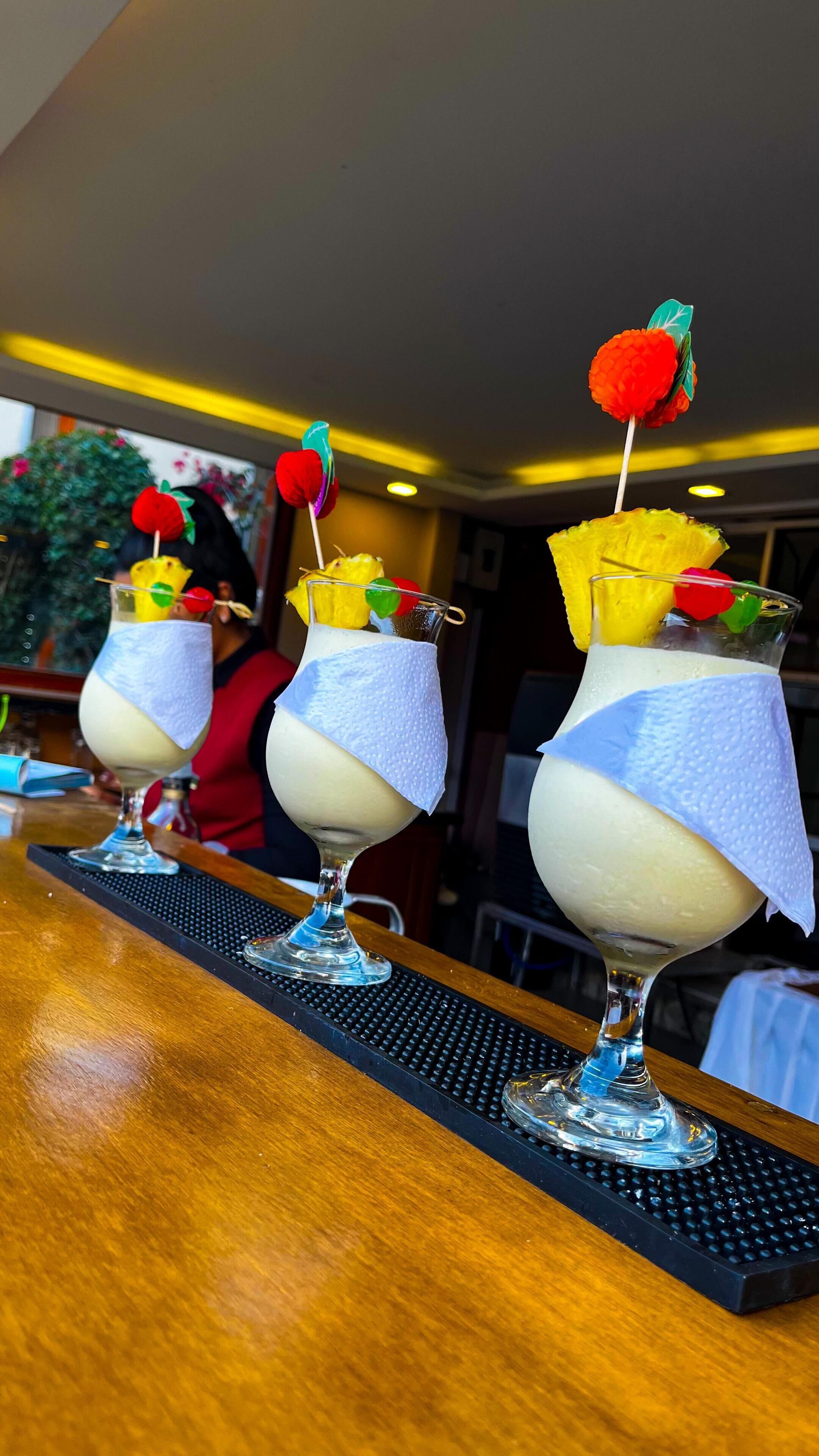 Three dessert drinks with fruit garnishes on a bar counter.