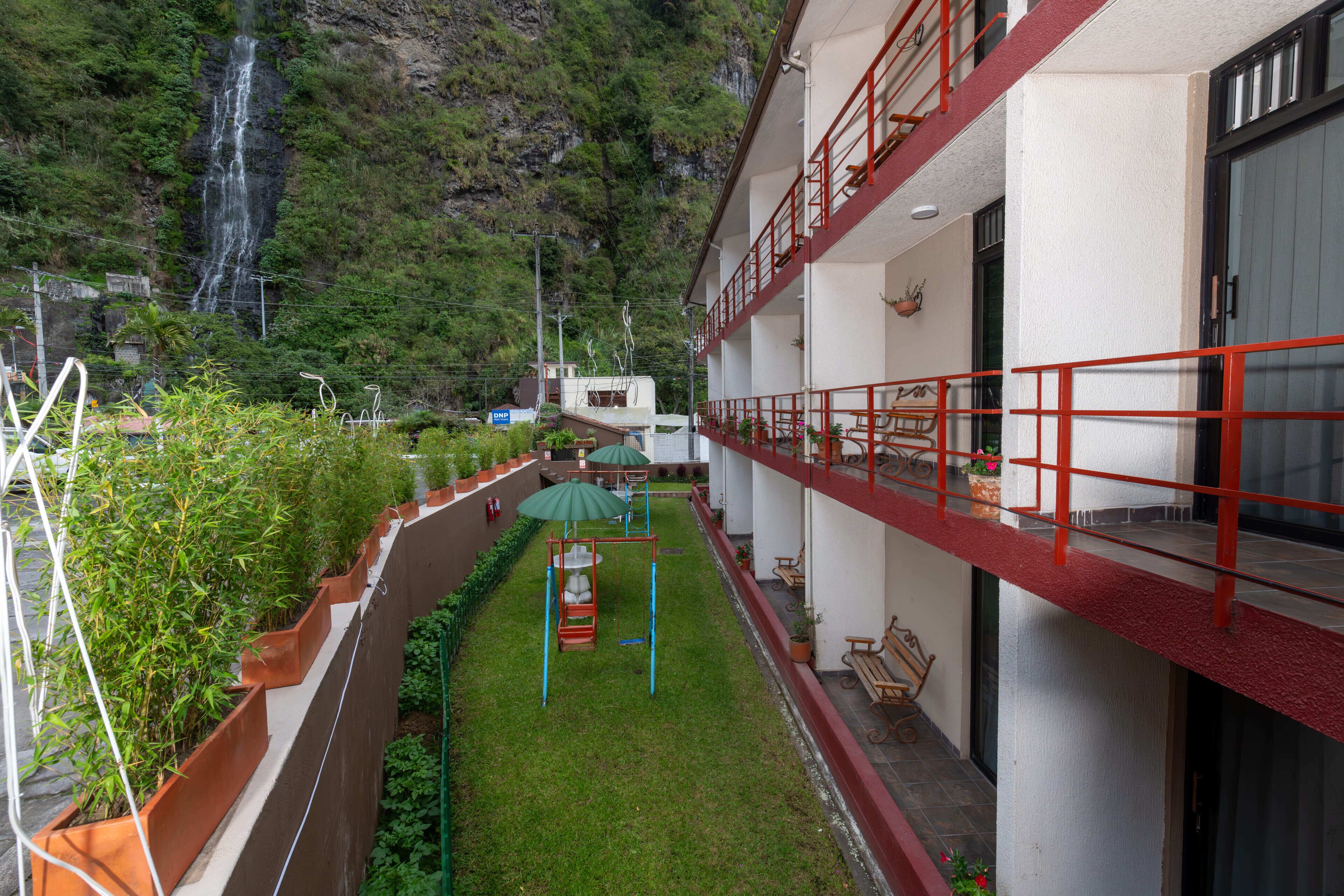 A hotel courtyard with a waterfall, green plants, a swing set, and outdoor seating.