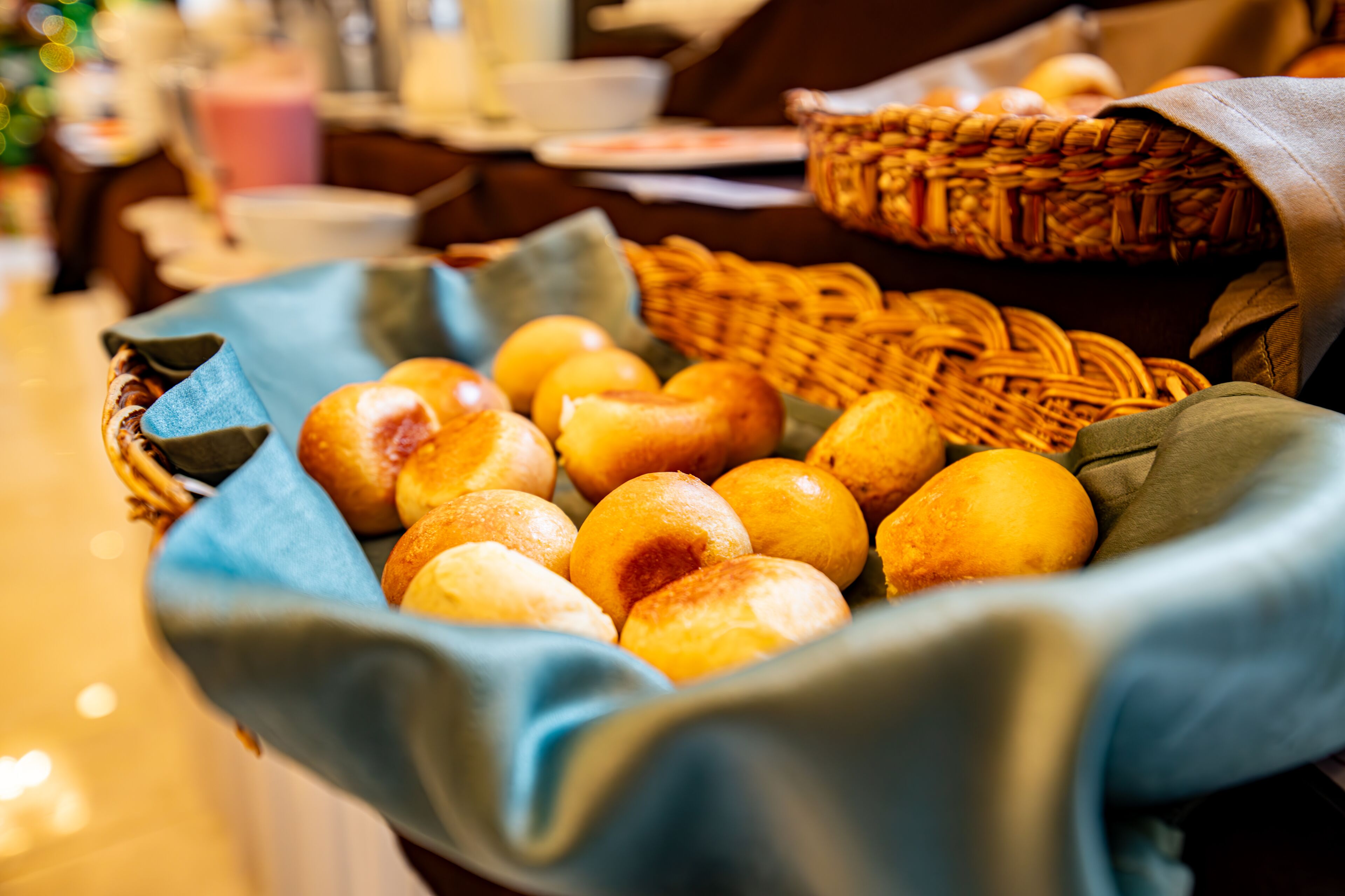 A basket filled with various baked goods, possibly bread or rolls, placed on a table with a blue cloth.