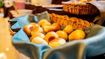 A basket filled with various baked goods, possibly bread or rolls, placed on a table with a blue cloth.