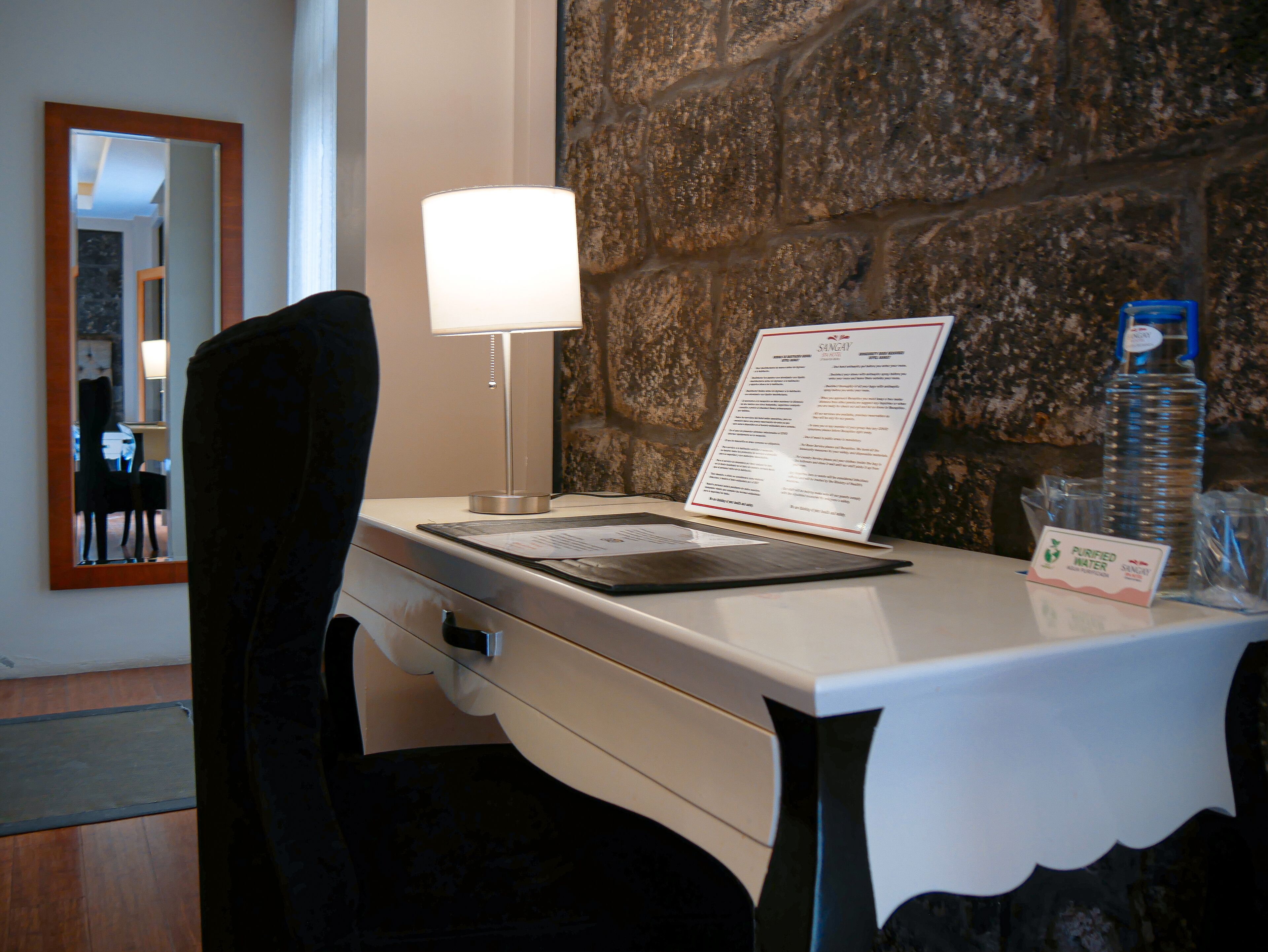 Una habitación de hotel con escritorio, lámpara, carta y dispensador de agua.