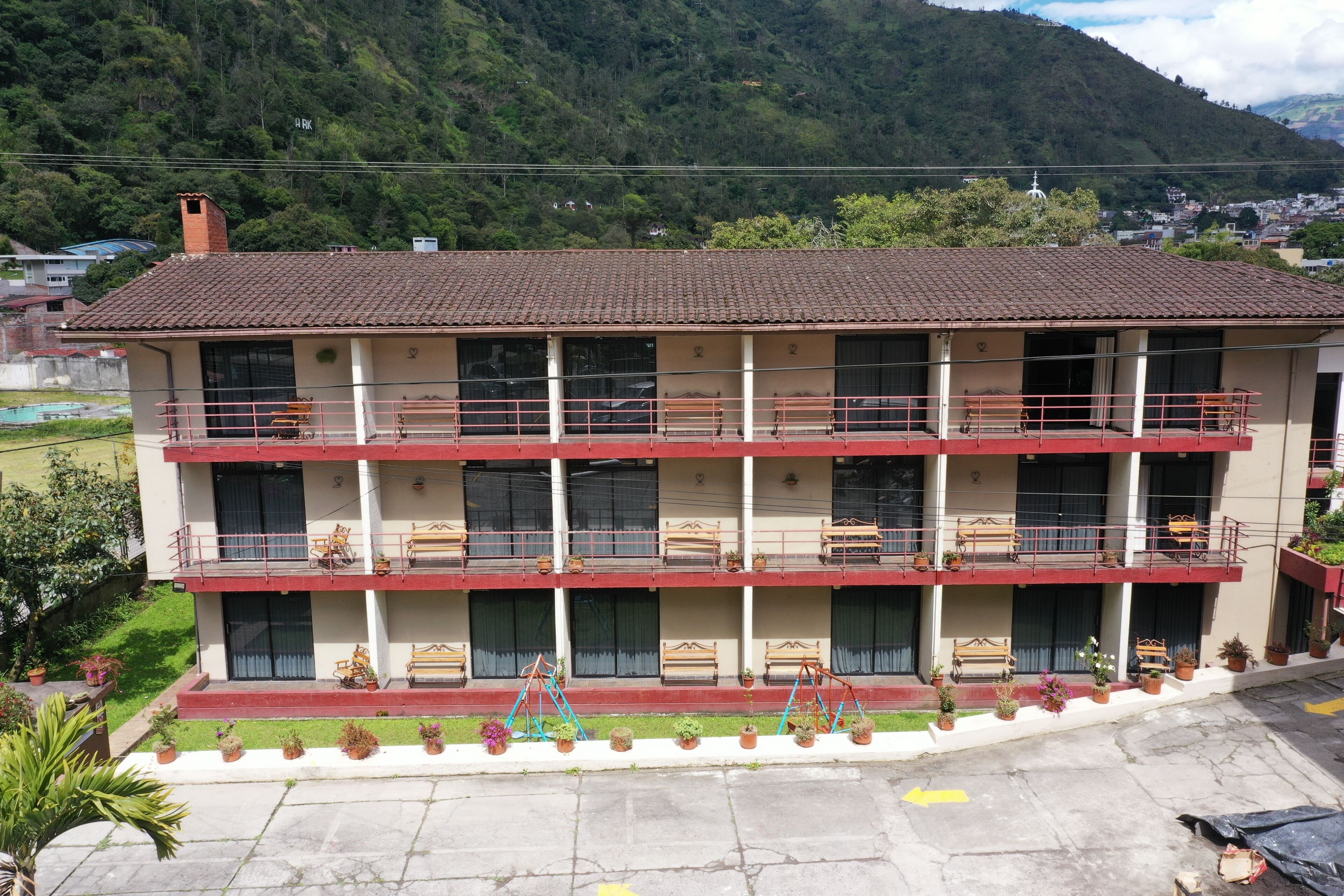 Un edificio de varios pisos con balcones, plantas en macetas y vistas a una zona montañosa.