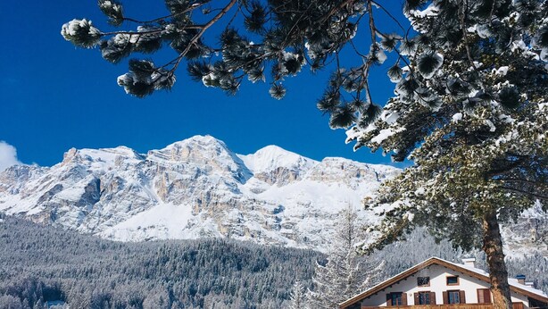 Eine verschneite Berglandschaft mit einer Holzhütte, die Balkone und ein schneebedecktes Dach besitzt.