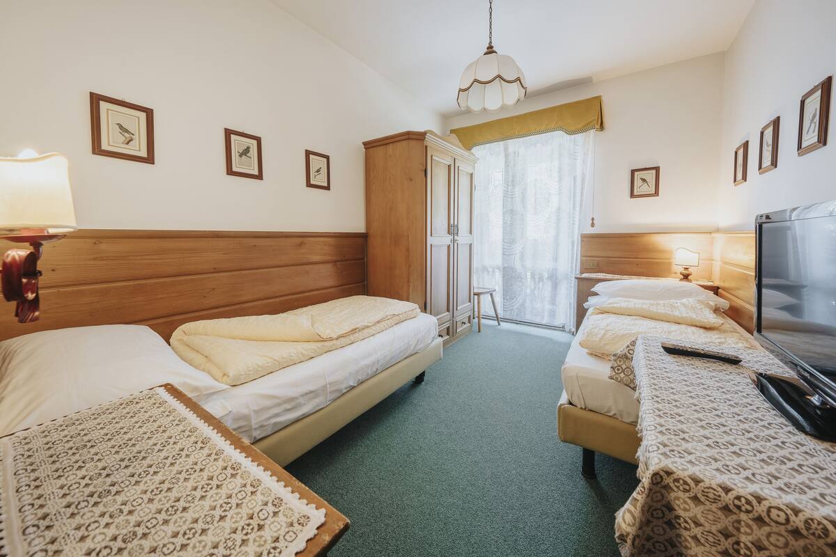 A hotel room with two single beds, a wooden wardrobe, a television, and a window with curtains.