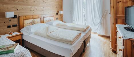 A bedroom with a wooden headboard, a bed with white linens, a nightstand with a lamp, and a wooden wardrobe with a TV.
