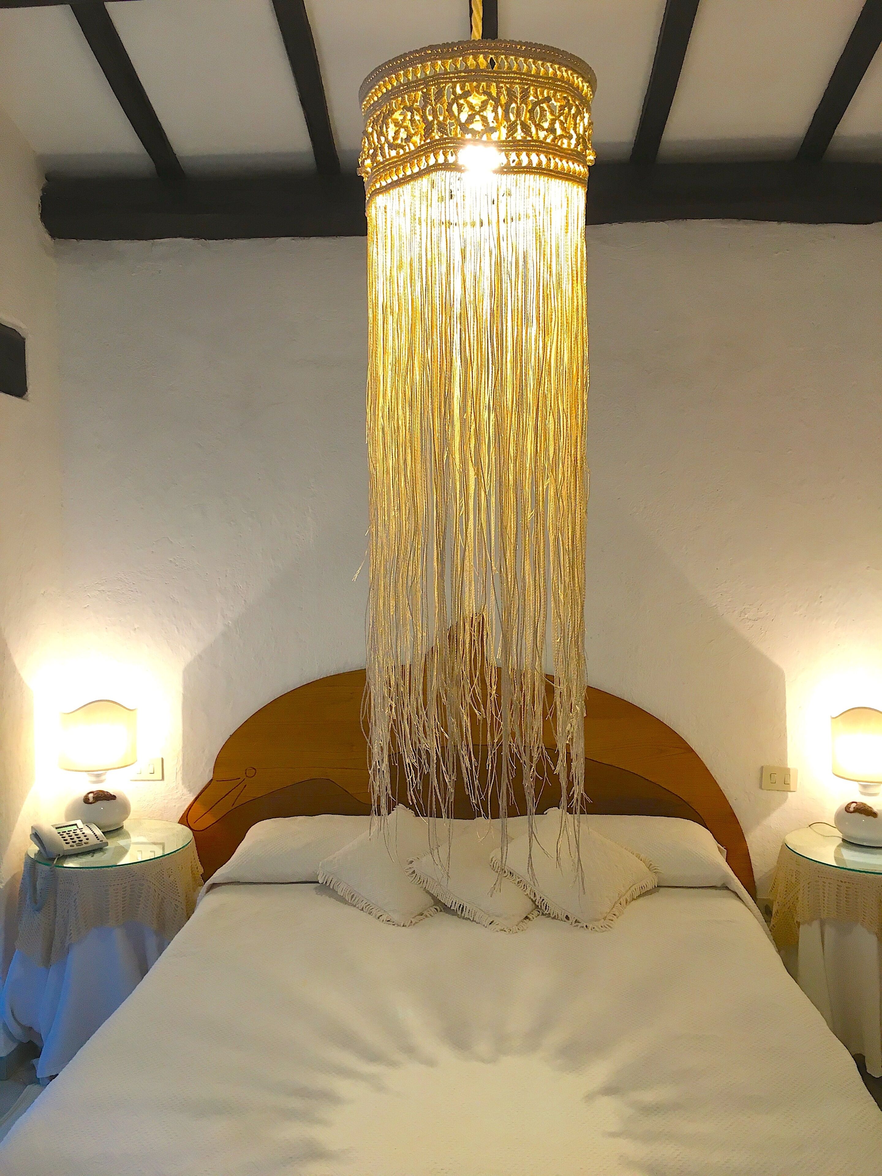 Uma cama com luminária pendente, duas mesas de cabeceira com abajures e uma cabeceira de madeira.