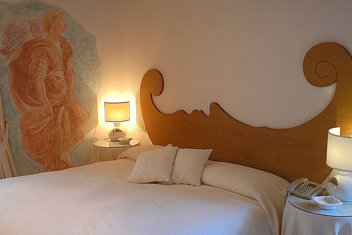 Een hotelkamer met een bed, een nachtkastje met een lamp, een telefoon aan de muur en een schilderij.