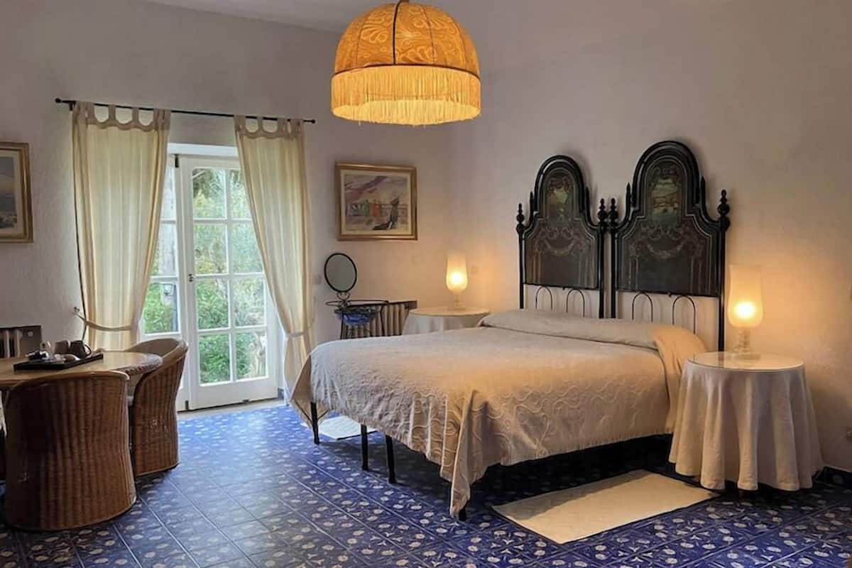 Een slaapkamer met een bed, twee nachtkastjes, een stoel, een raam met gordijnen en een hanglamp.