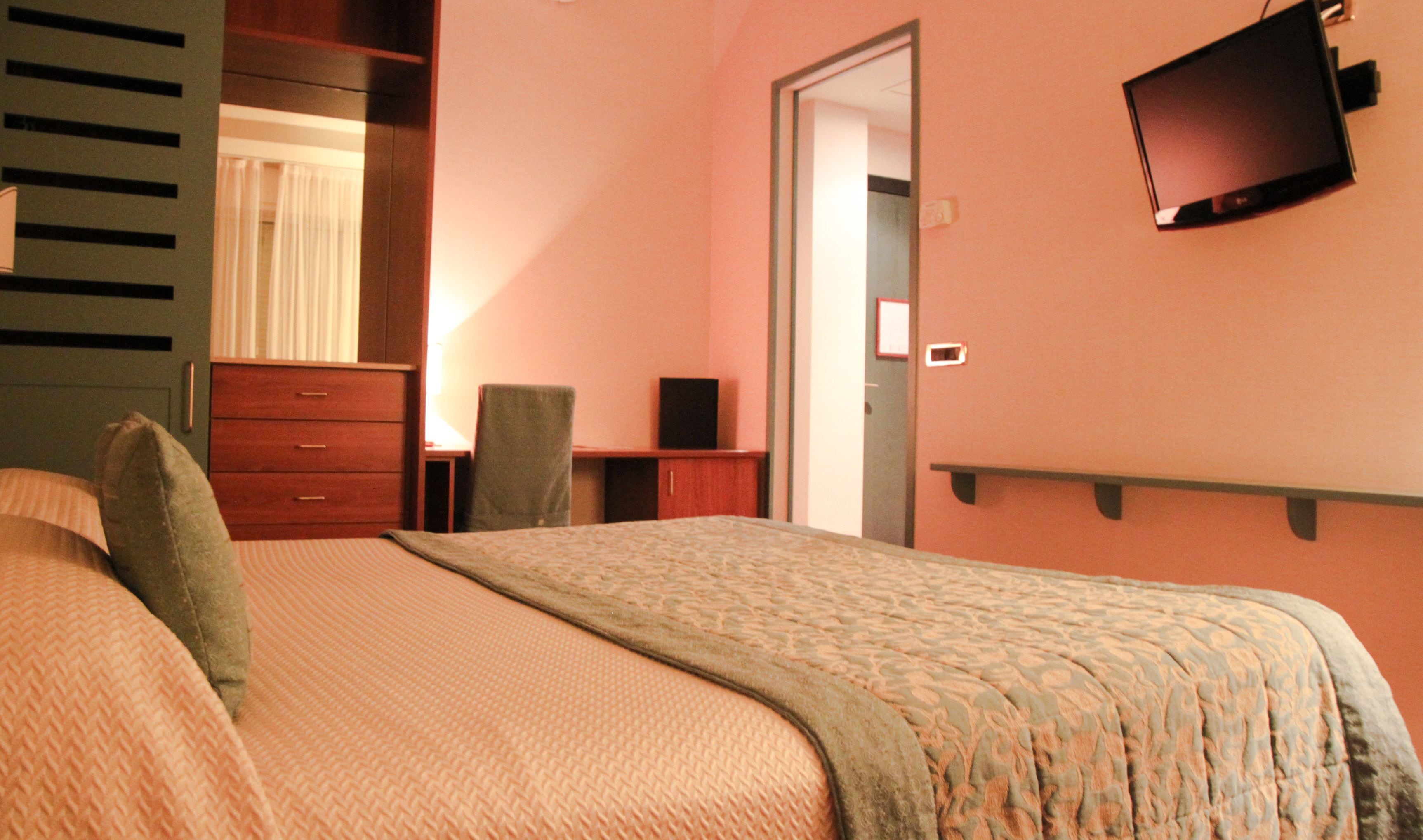 A hotel room with a bed, a desk, a chair, a television, and a wardrobe.