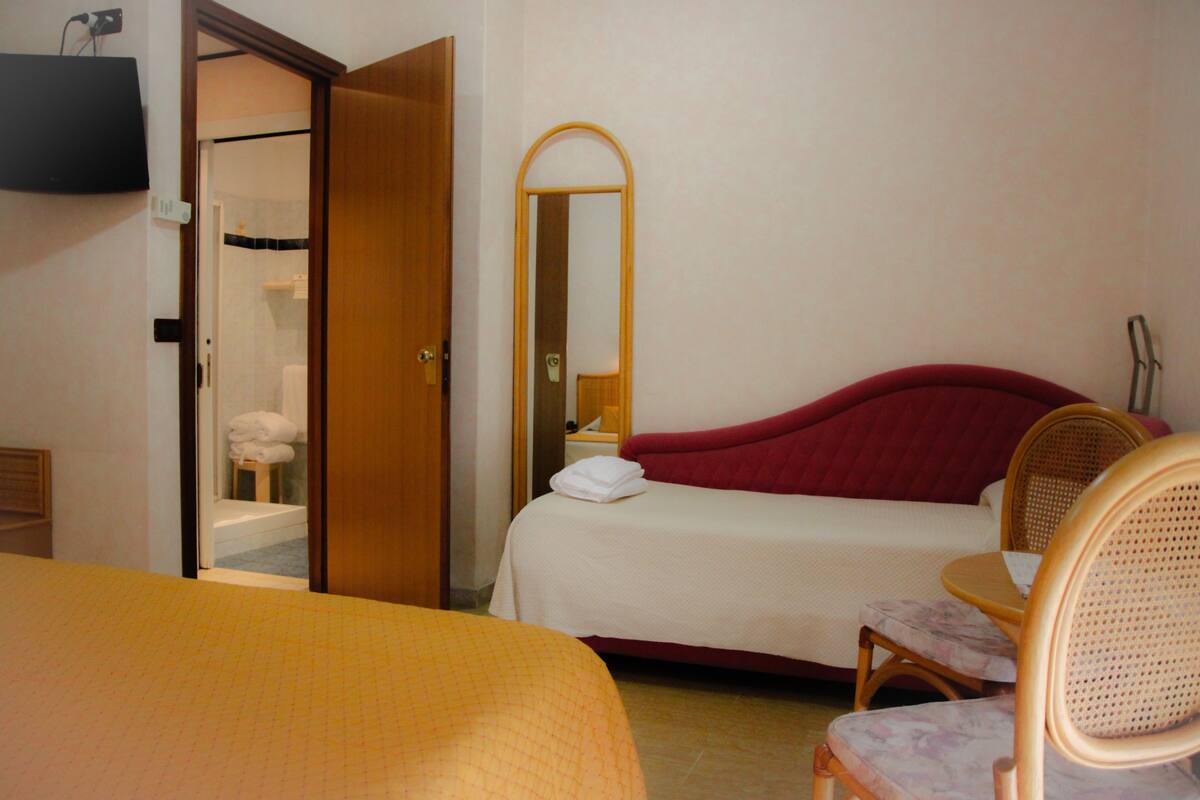 A hotel room with a bed, a chair, a mirror, and a bathroom visible through an open door.