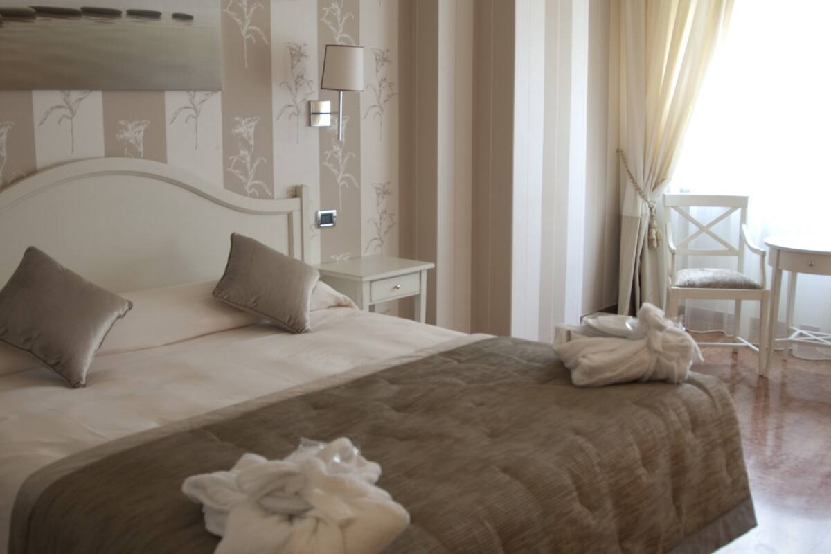 A neatly arranged hotel room with a large bed, a bedside table, a chair, and a lamp.