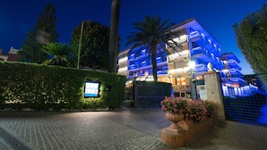 A multi-story hotel with a modern design, featuring a gated entrance and a landscaped area with a palm tree and flowers. - Hotel Garden Lido (Loano)