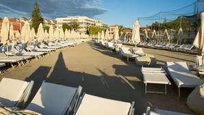 A beachside hotel with rows of sun loungers and umbrellas, a sandy walkway, and buildings in the background. - Hotel Garden Lido (Loano)