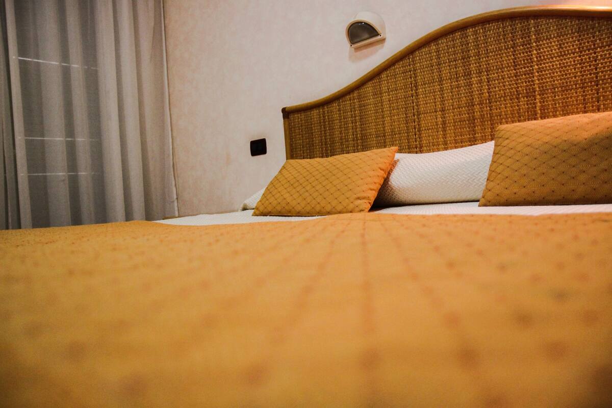 A bed with a headboard, two pillows, and a window with curtains.