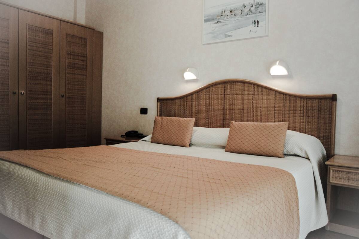 A bedroom with a large bed, two bedside tables, a nightstand, and a wardrobe.