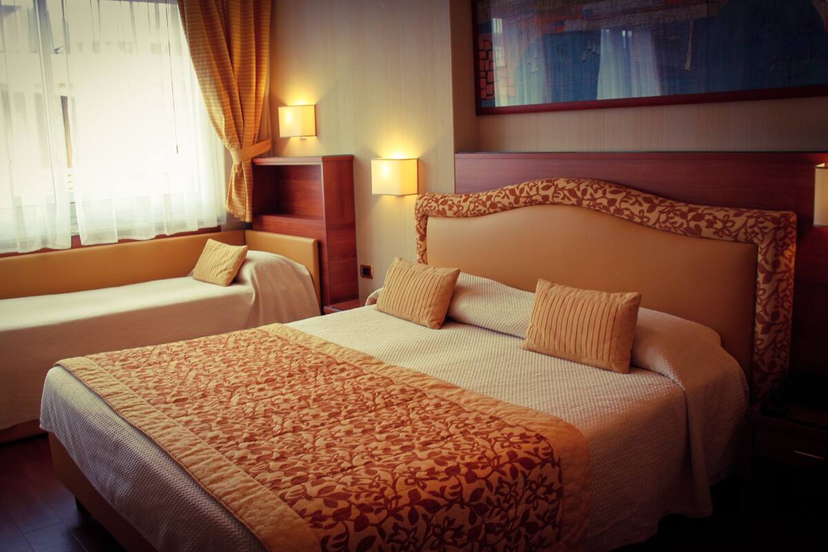 A hotel room with two beds, a nightstand, and a lamp.