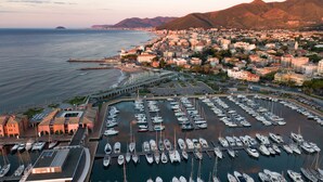 A marina with numerous boats docked, a coastal town with buildings, and mountains in the background. - Hotel Garden Lido (Loano)