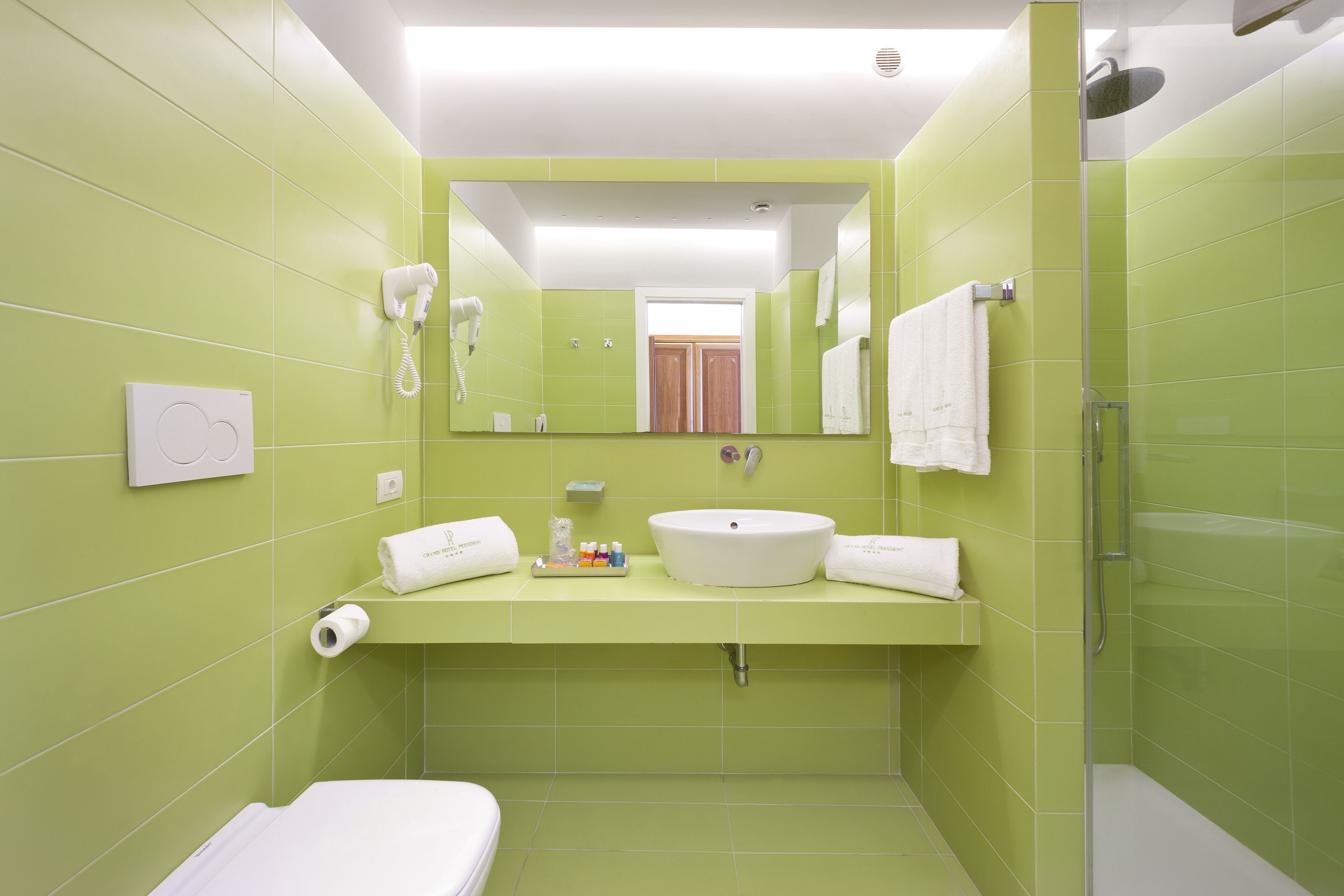 A bathroom with green tiles, a white sink, a hairdryer, and a shower.