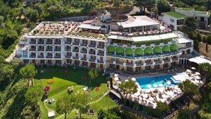 Un gran hotel con múltiples balcones, piscina y exuberante jardinería.