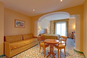 Una habitación de hotel con sofá, cama, mesa redonda con sillas, televisor y un cuadro en la pared.