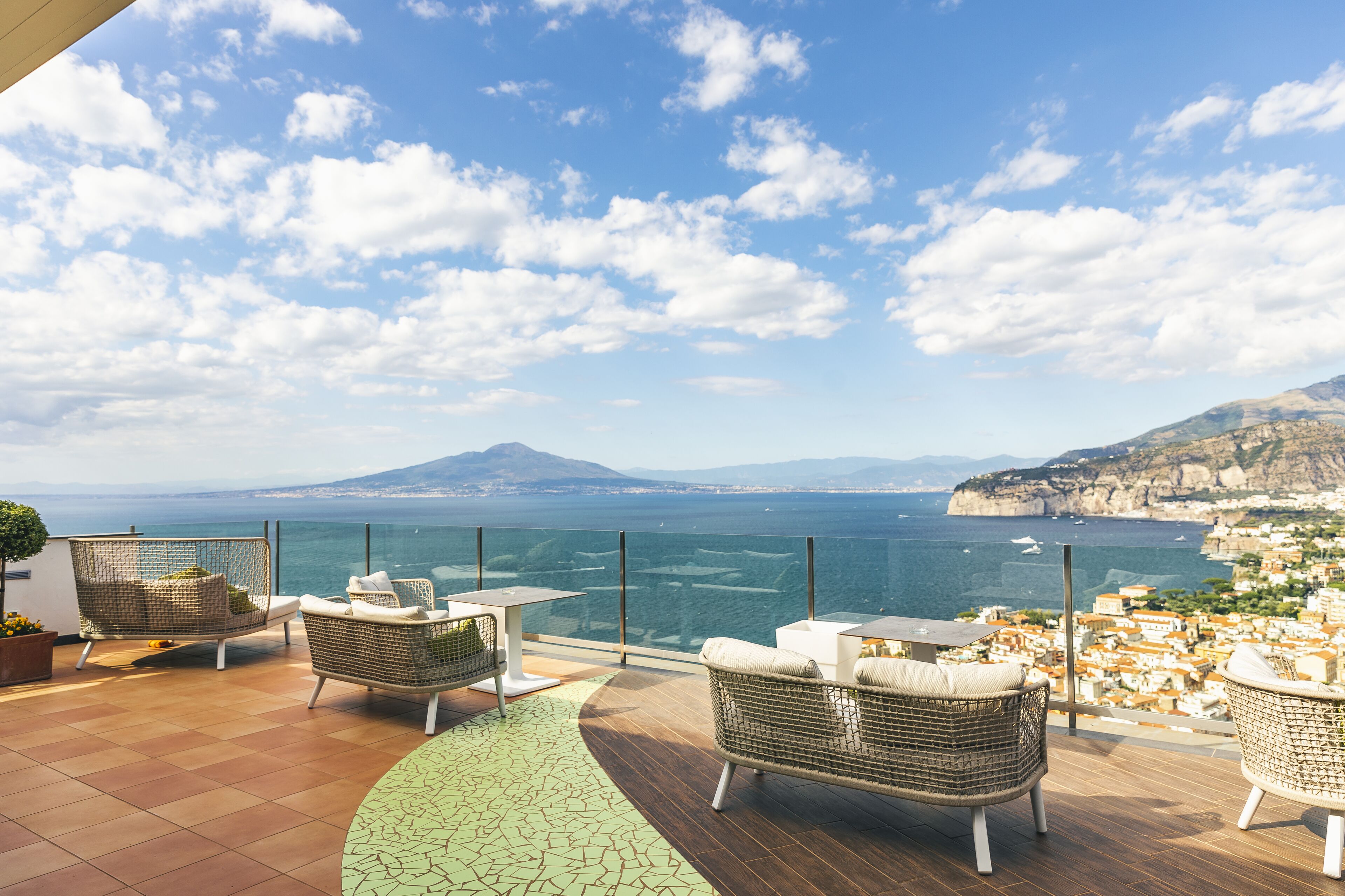 A terrace with wicker furniture and a view of the sea and a distant mountain.