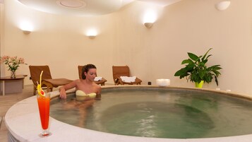 A woman in a spa pool with lounge chairs and a potted plant.