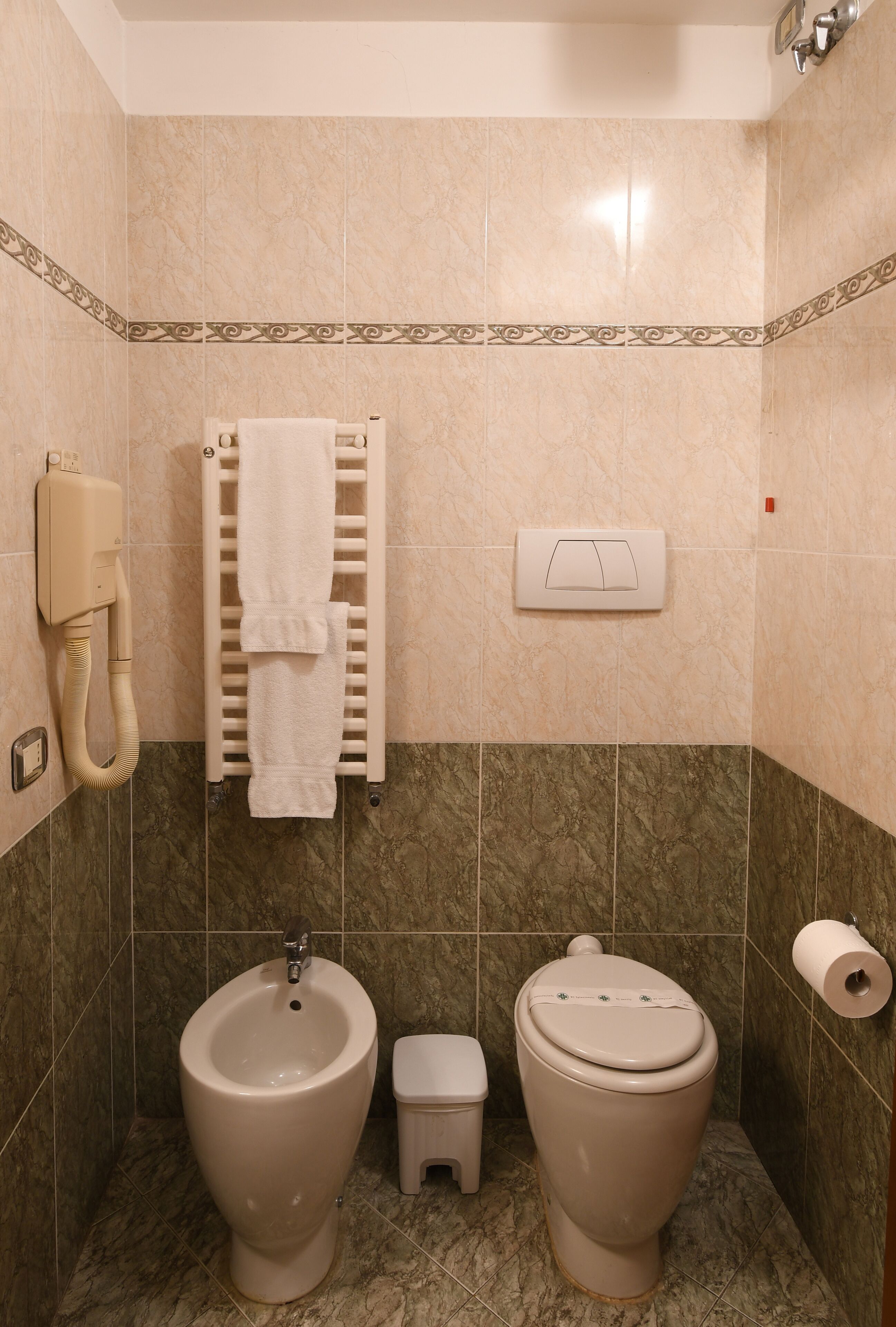 Ein Badezimmer mit einem Bidet, WC, Handtuchwärmer und Toilettenpapierhalter.