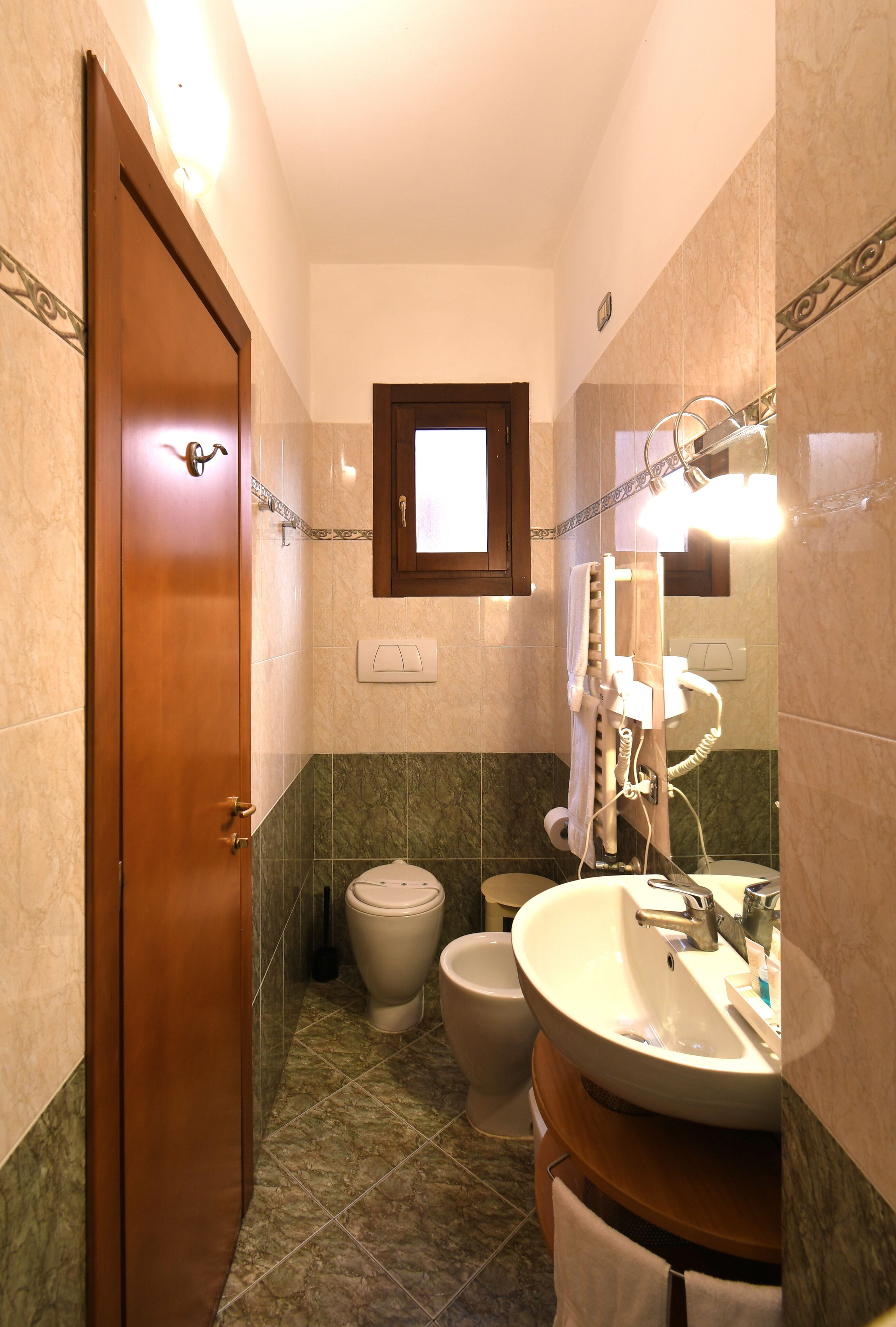 A bathroom with a wooden door, a toilet, a bidet, and a sink with a mirror.