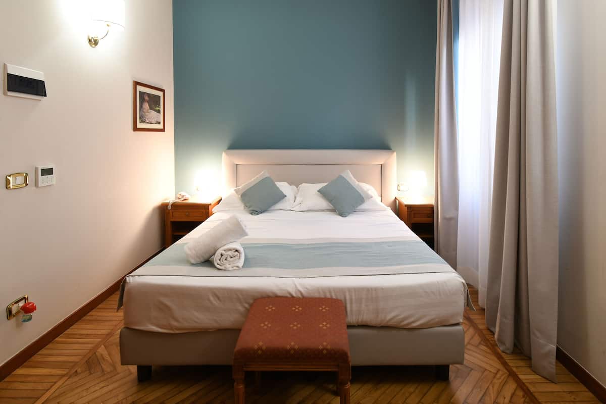 A neatly made bed with pillows, a bedside table, a wall-mounted light, and a wooden floor.