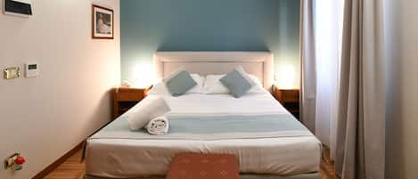 A neatly made bed with pillows, a bedside table, a wall-mounted light, and a wooden floor.