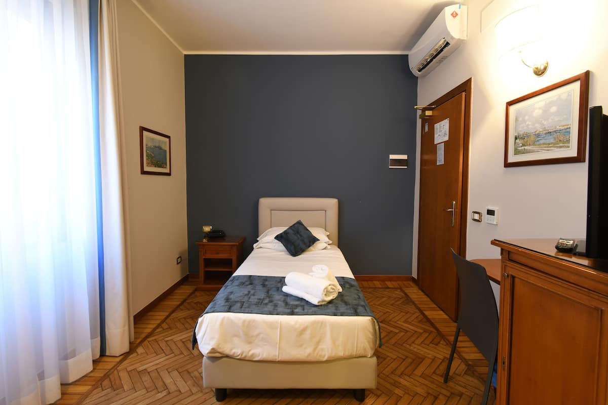 A hotel room with a bed, bedside table, and a desk with a chair.