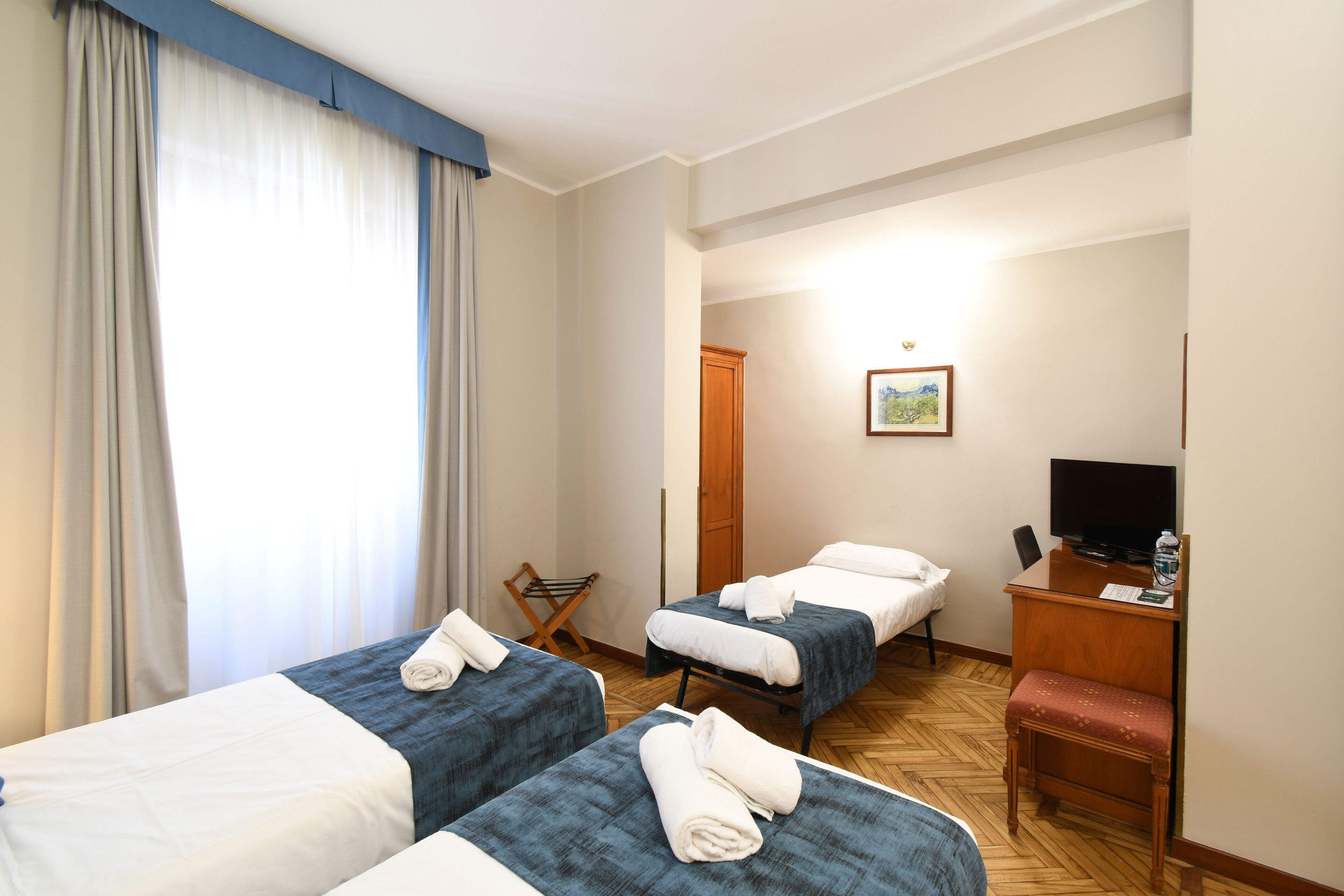 Une chambre d’hôtel avec deux lits, un bureau avec une télévision et une chaise.