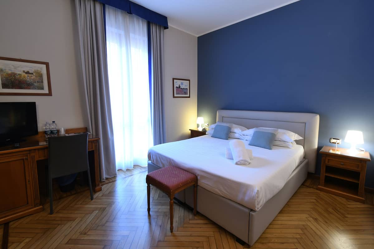 A hotel room with a large bed, a desk with a chair, a television, and a window with curtains.
