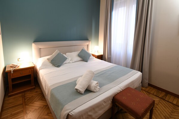 A neatly made bed with pillows, a bedside table with a lamp, and a wooden floor.