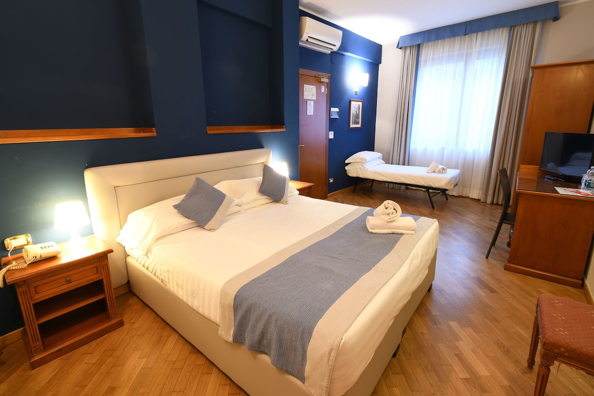 A hotel room with a large bed, bedside tables, a desk, a chair, and a television.